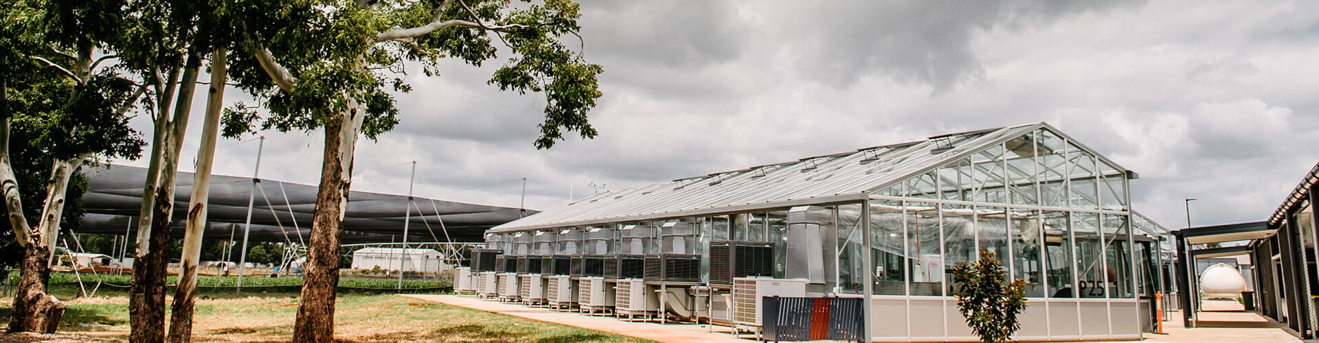 Modern greenhouse with adjacent outdoor hvac units under a cloudy sky.