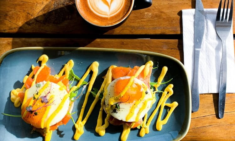 Two eggs benedict on a plate next to a cup of coffee.