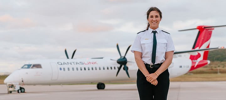 A female pilot standing in front of a qantaslink airplane on the tarmac.