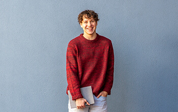 Noah standing in front of a blue wall, smiling at the camera.