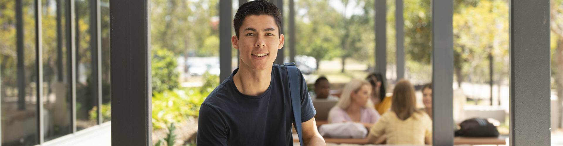 A young male university student sitting outside, smiling at the camera.