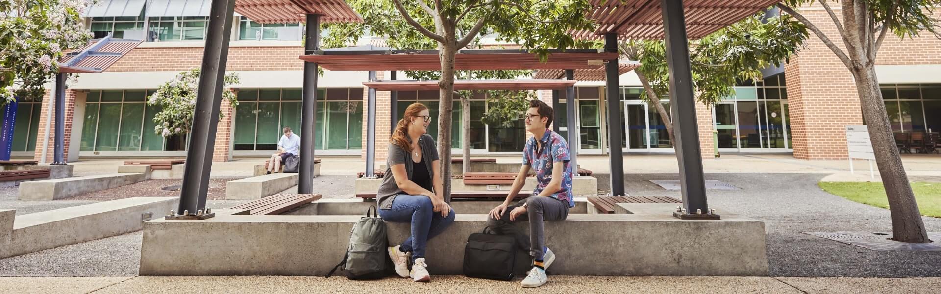 Two individuals sitting and conversing in a campus courtyard.