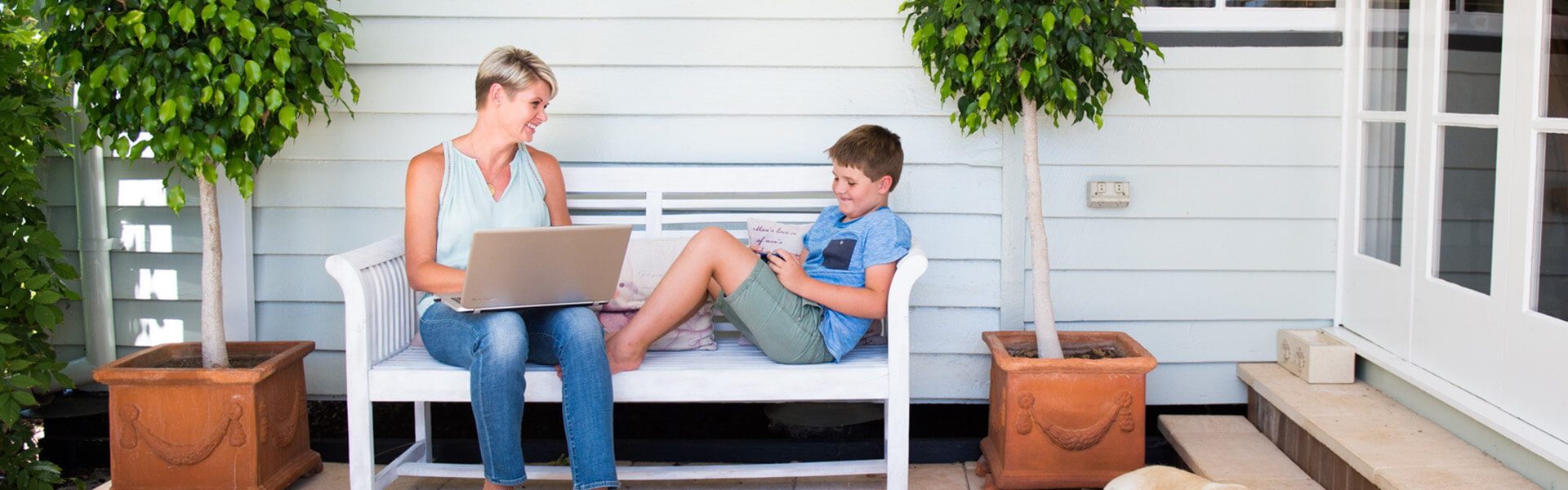 Mother studying with laptop on a bench with her son playing beside her.