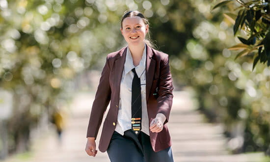 A female high school student walking in a park, smiling at the camera.