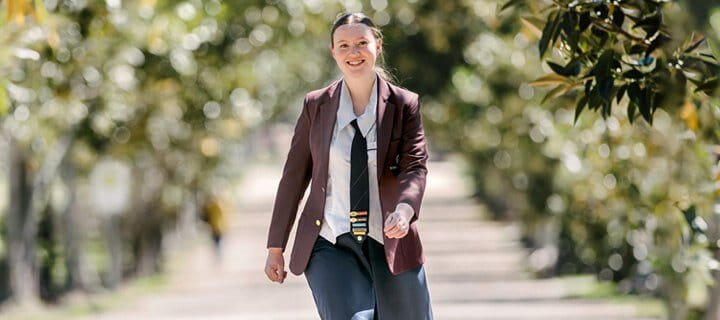 Female high school student, walking on a path in a park, smiling at the camera.