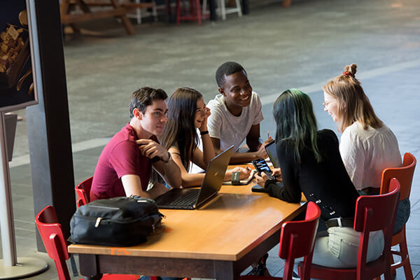 Group of students engaged in discussion around a laptop at a campus setting.