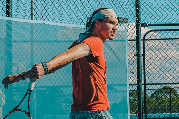 Tennis player mid-swing with focused expression on outdoor court.